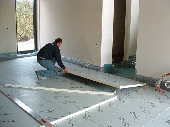 Installateur posant des isolants thermiques pour le sol sur un chantier intérieur, déroulant des panneaux sur une surface protégée