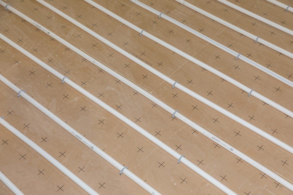 Réseaux de chauffage au sol en installation, panneaux isolants beige avec repères en croix, guide pour réduire sa consommation thermique.